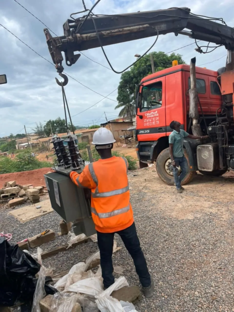 Technicien guidant un transformateur de distribution soulevé par le bras de grue d'un camion