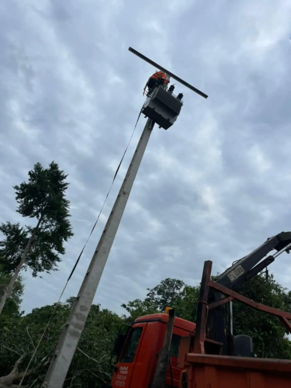 Technicien fixant un transformateur en haut d'un poteau électrique en béton, camion-grue au pied