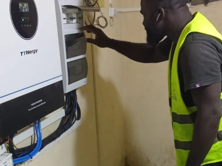Technicien en gilet haute visibilité intervenant sur un coffret électrique à côté d'un onduleur solaire