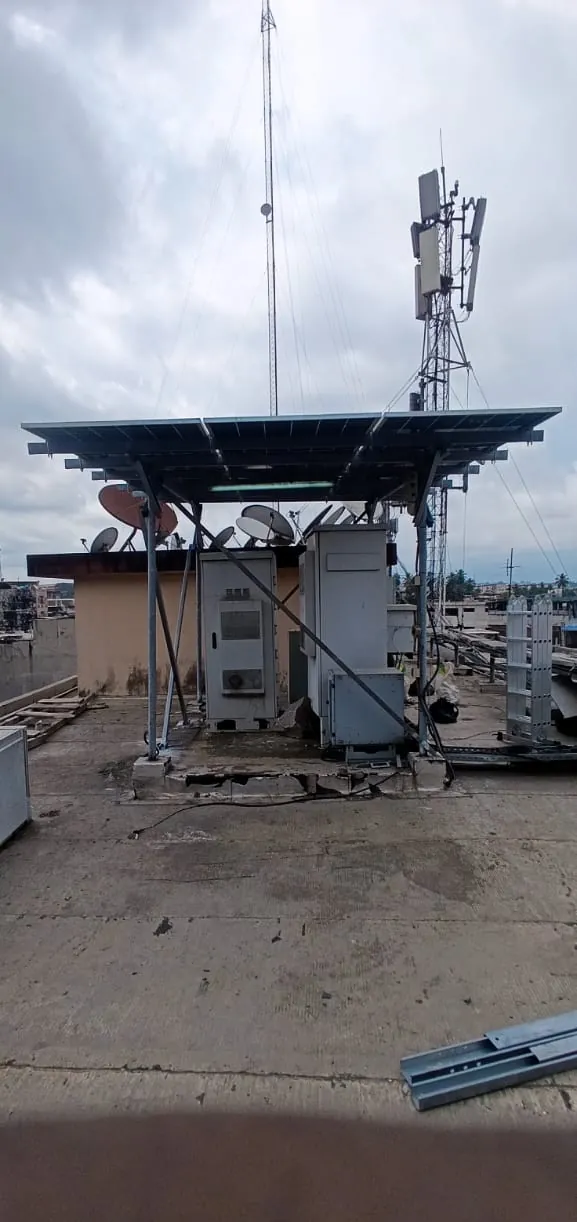 Site télécom en toiture : armoires sous un auvent de panneaux solaires, pylône et antennes en arrière-plan
