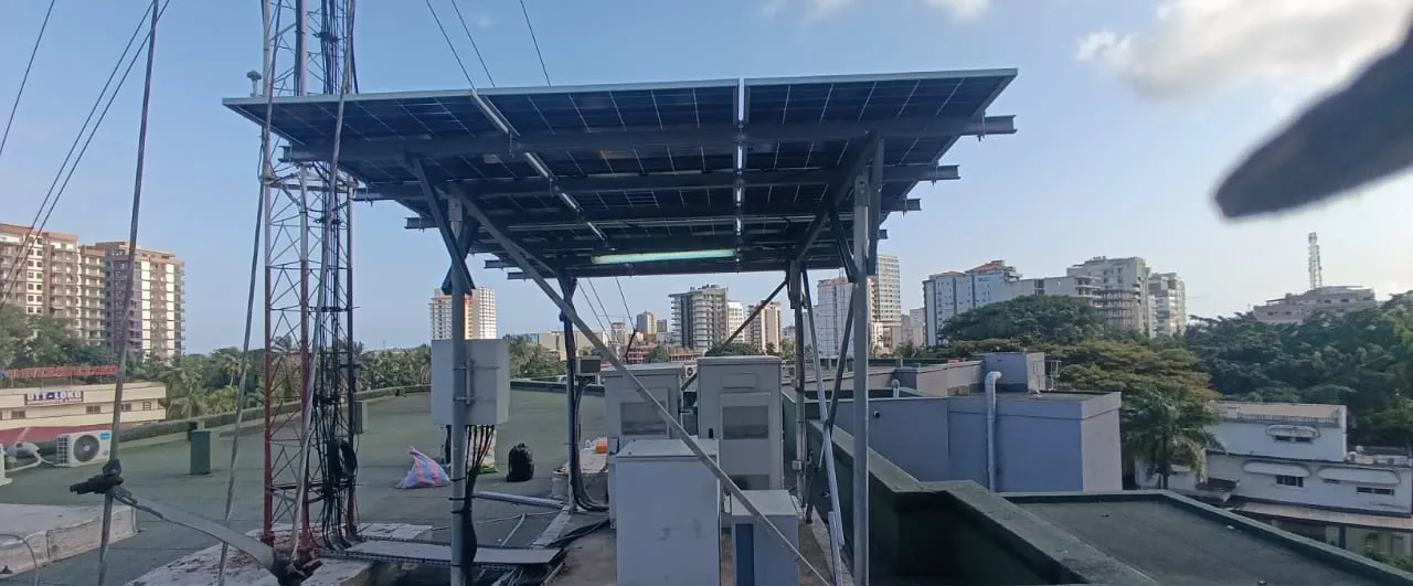 Site télécom en terrasse : armoires d'équipements sous un auvent solaire, à côté d'un pylône