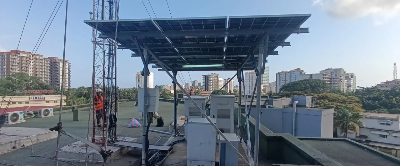 Technicien équipé d'un harnais montant sur un pylône télécom, à côté des armoires du site